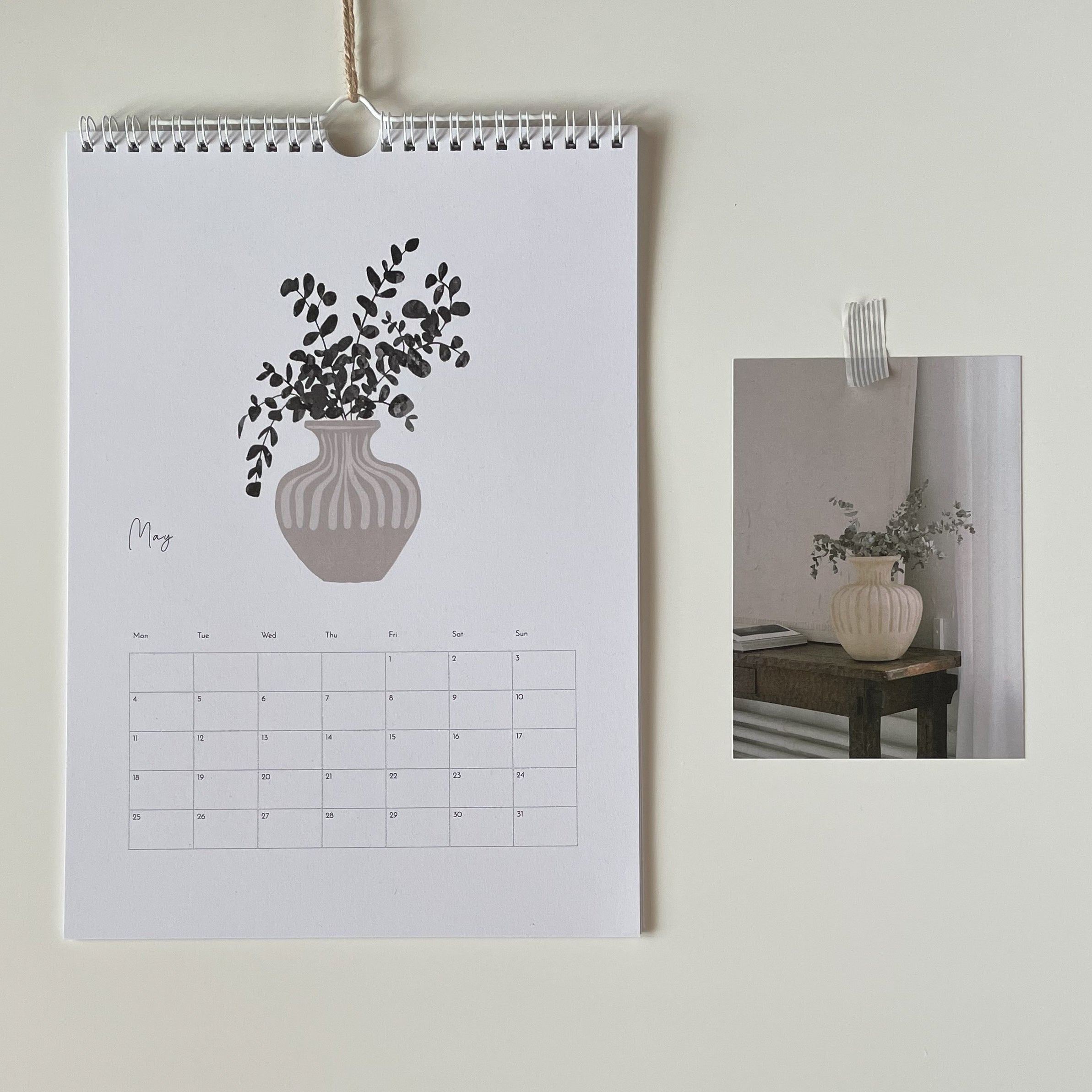 Calendar with a vase and plant illustration on a wall, with a smaller inset photo of a similar setup.