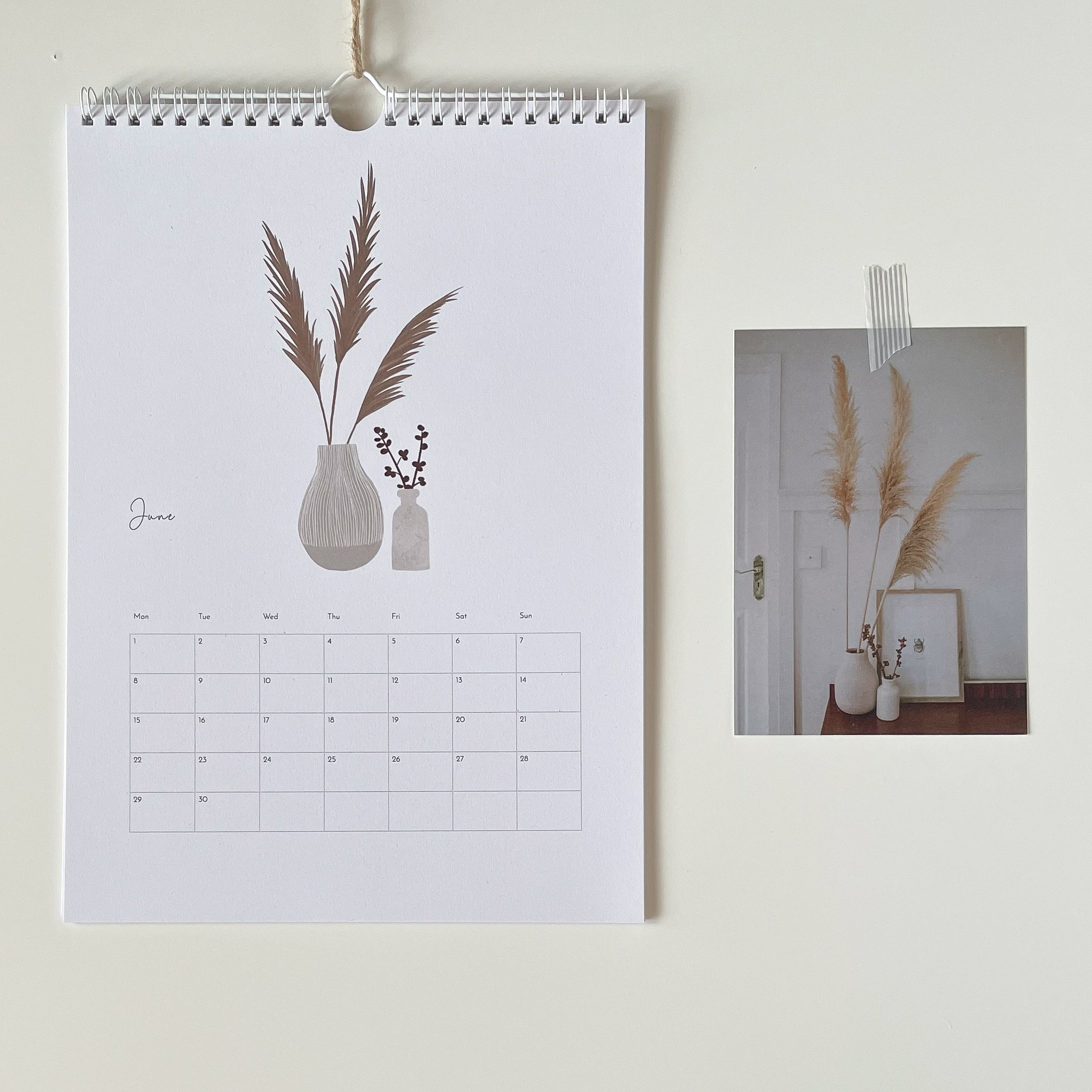 Wall calendar with decorative design of vases and plants on a white wall.