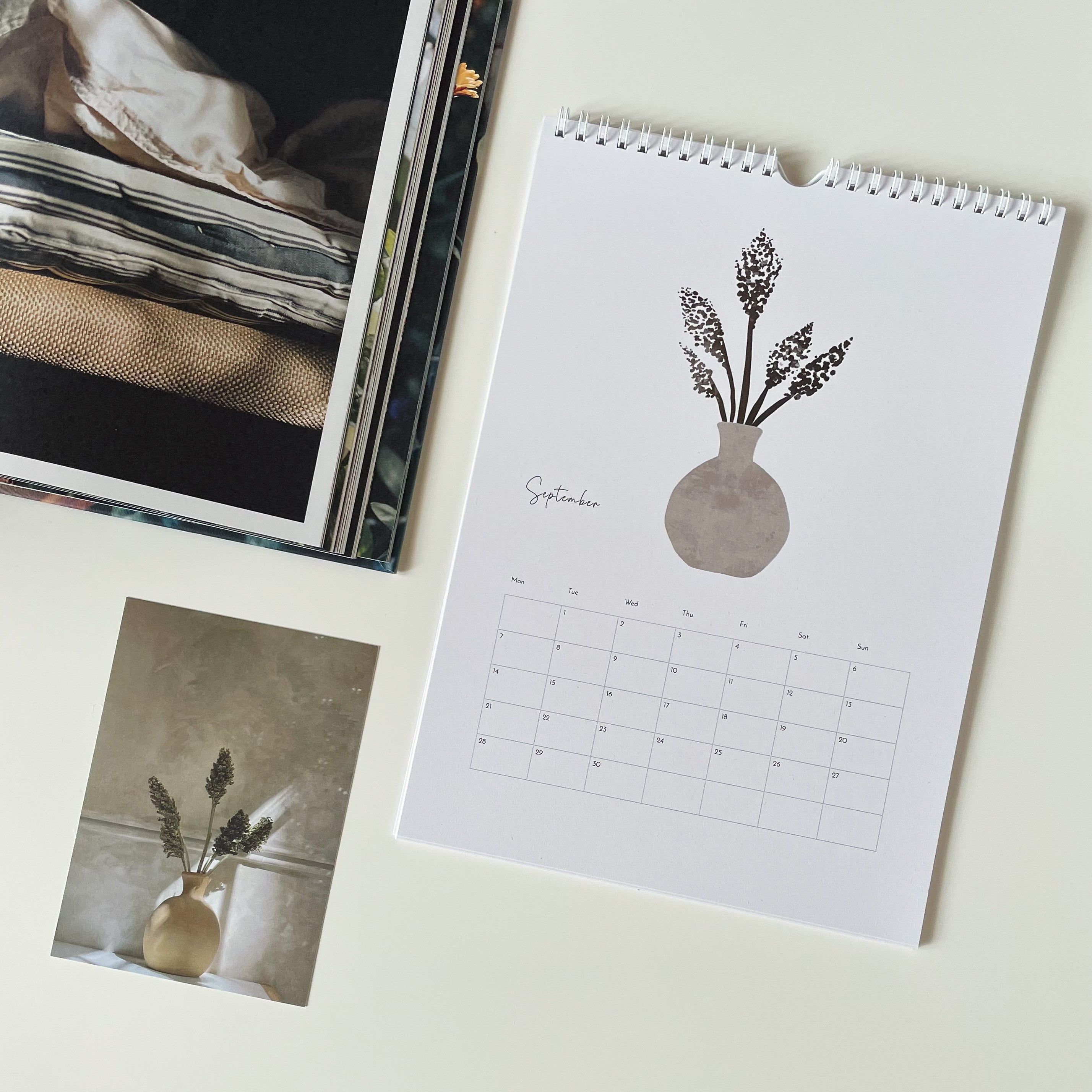 Minimalist calendar with floral vase design on a light surface next to a photo album.
