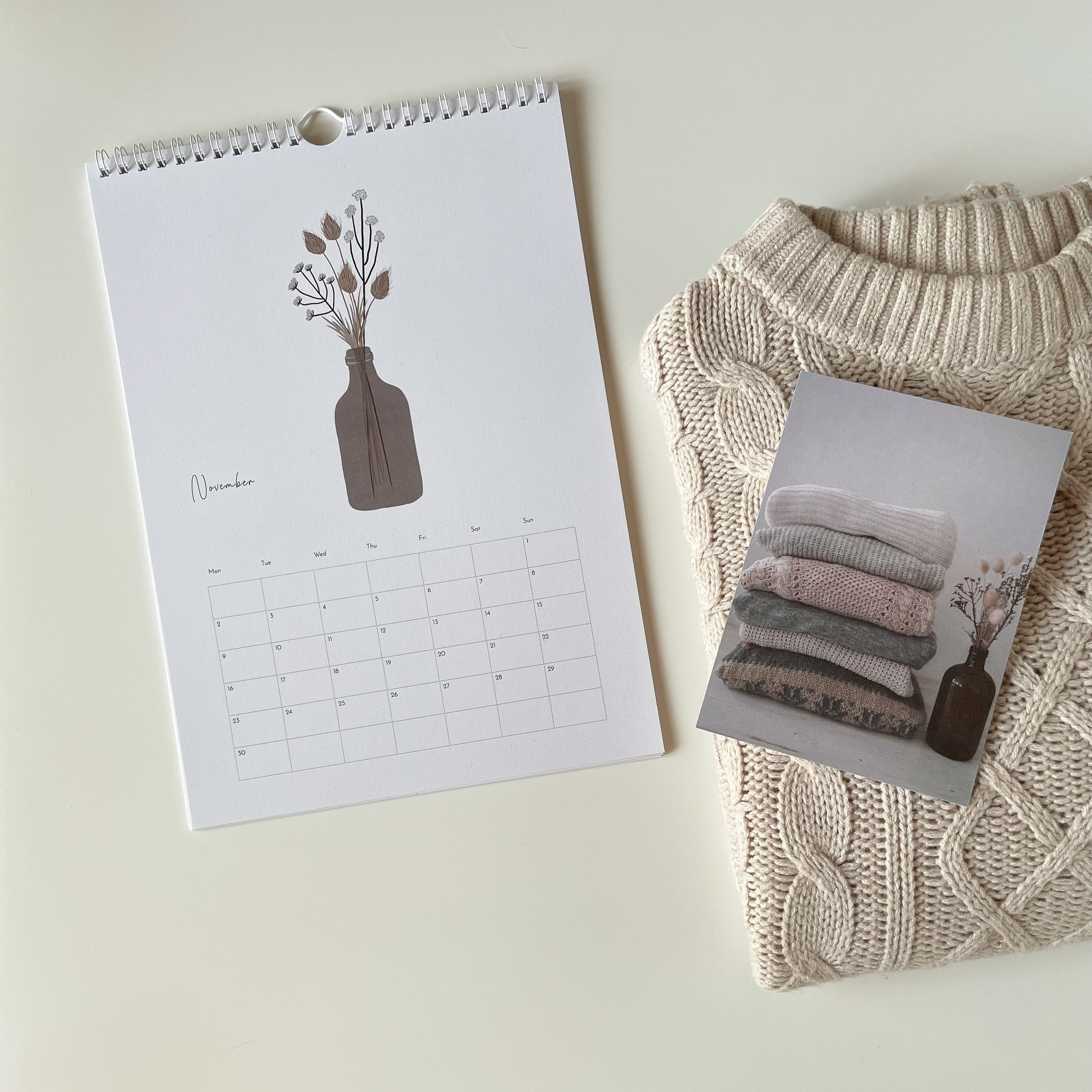 Calendar with a vase design next to a beige sweater and photo postcard on a light background