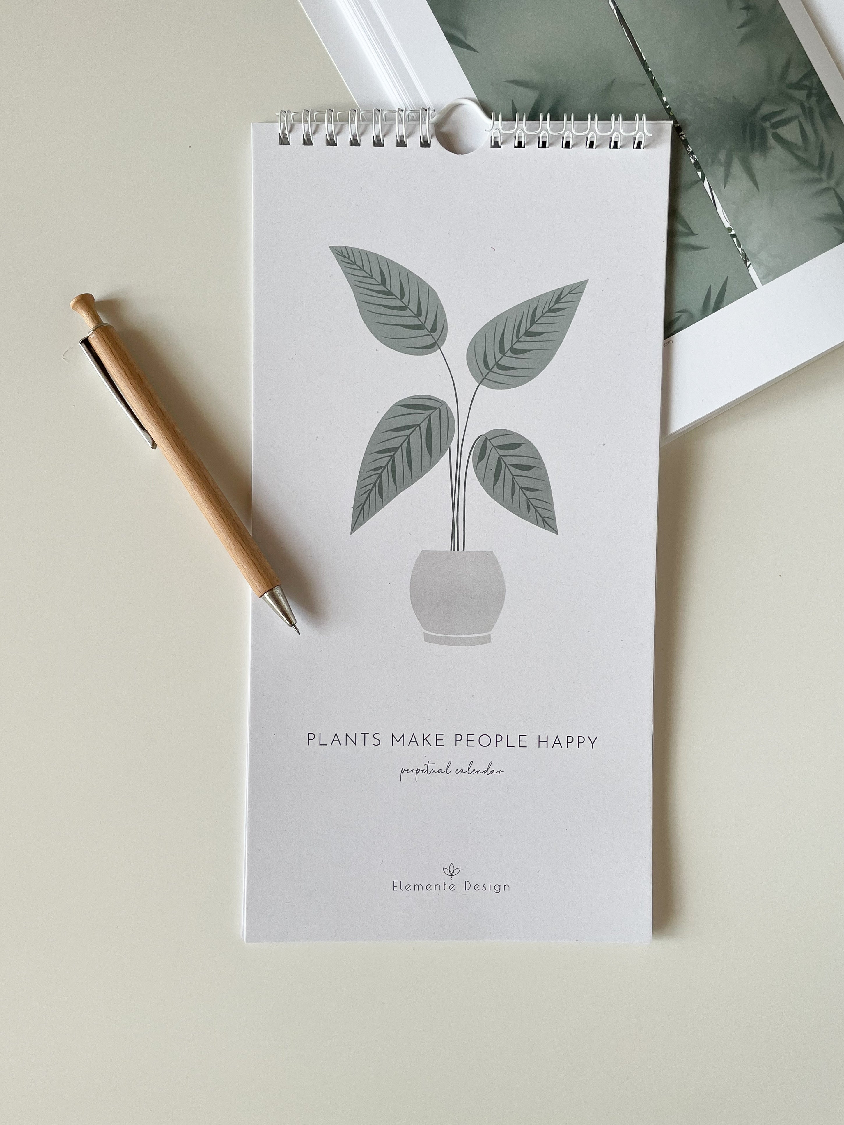 Small spiral-bound calendar with plant design and 'Plants Make People Happy' text on a light surface.